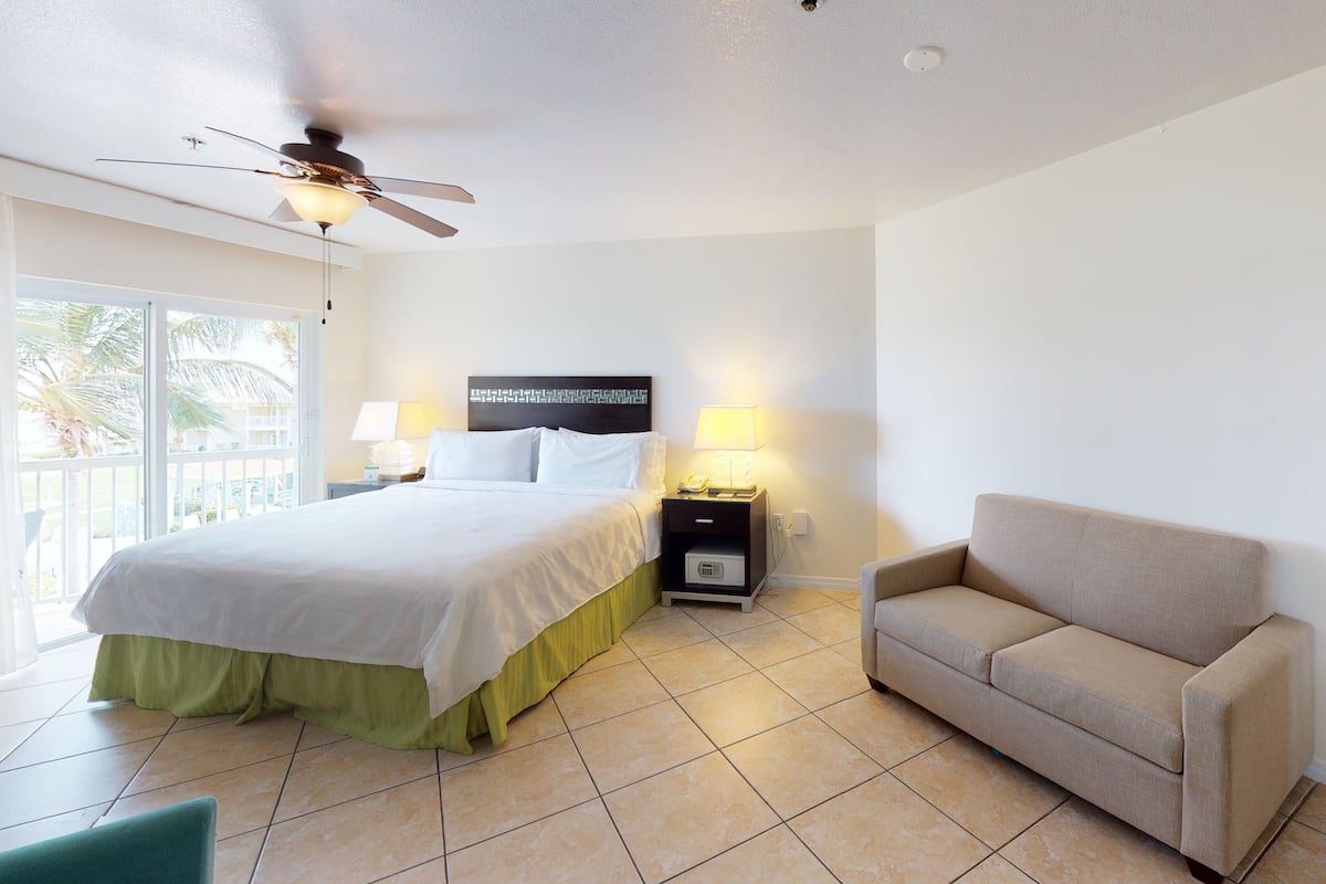 A hotel room with a bed, a nightstand, a lamp, a sofa, and a ceiling fan.