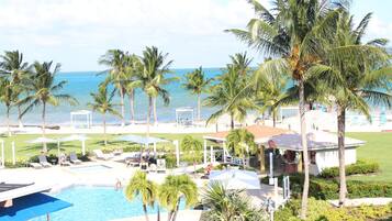 A resort with a pool, lounge chairs, palm trees, and a view of the ocean.