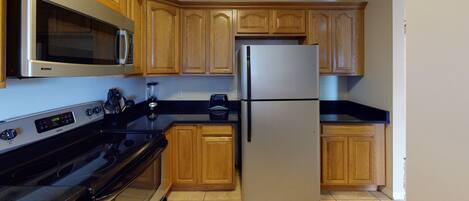 A kitchen with wooden cabinets, a stainless steel refrigerator, a microwave, and a black stove.