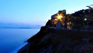 Un edificio frente al mar con balcón, vistas al océano, una escalera destacada y un pequeño jardín.