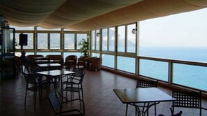 Ein Restaurant mit Tischen, Stühlen, großen Fenstern und Blick aufs Meer.
