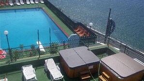 Poolbereich mit Liegestühlen und einem kleinen Gebäude, vermutlich eine Sauna oder Umkleidekabine, auf dem Deck eines Kreuzfahrtschiffs.