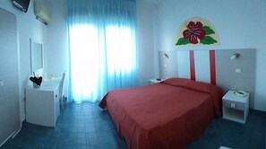 Una habitación de hotel con cama, escritorio, silla, espejo, mesita de noche y ventana con cortinas.