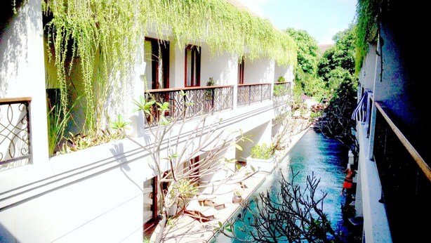 A building with a water feature, outdoor seating, and greenery. - Seminyak Lagoon All Suites Hotel (Keroboken Kelod)