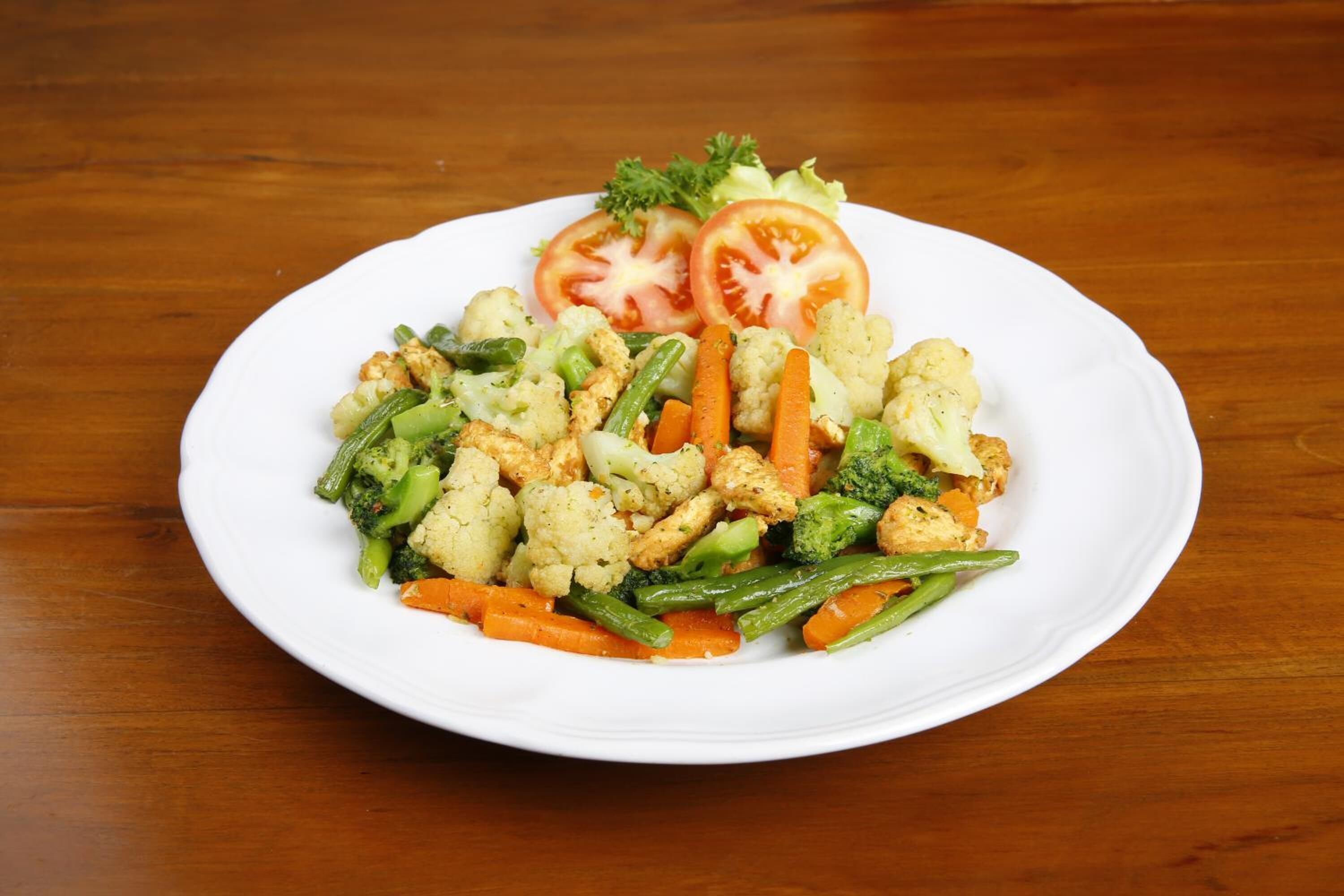 A white plate with a variety of vegetables including cauliflower, carrots, green beans, broccoli, and tomatoes on a wooden table.