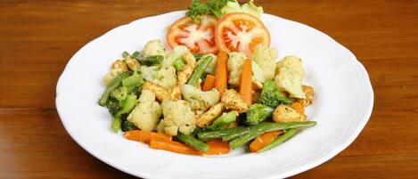 A white plate with a variety of vegetables including cauliflower, carrots, green beans, broccoli, and tomatoes on a wooden table.