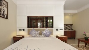 A bedroom with a large bed, two nightstands, a wooden headboard, a decorative mirror, and a small table with a plant. - Seminyak Lagoon All Suites Hotel (Keroboken Kelod)
