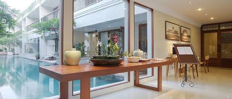 Un moderno vestíbulo de hotel con una amplia piscina de cristal, un mostrador de recepción de madera y un balcón con plantas.