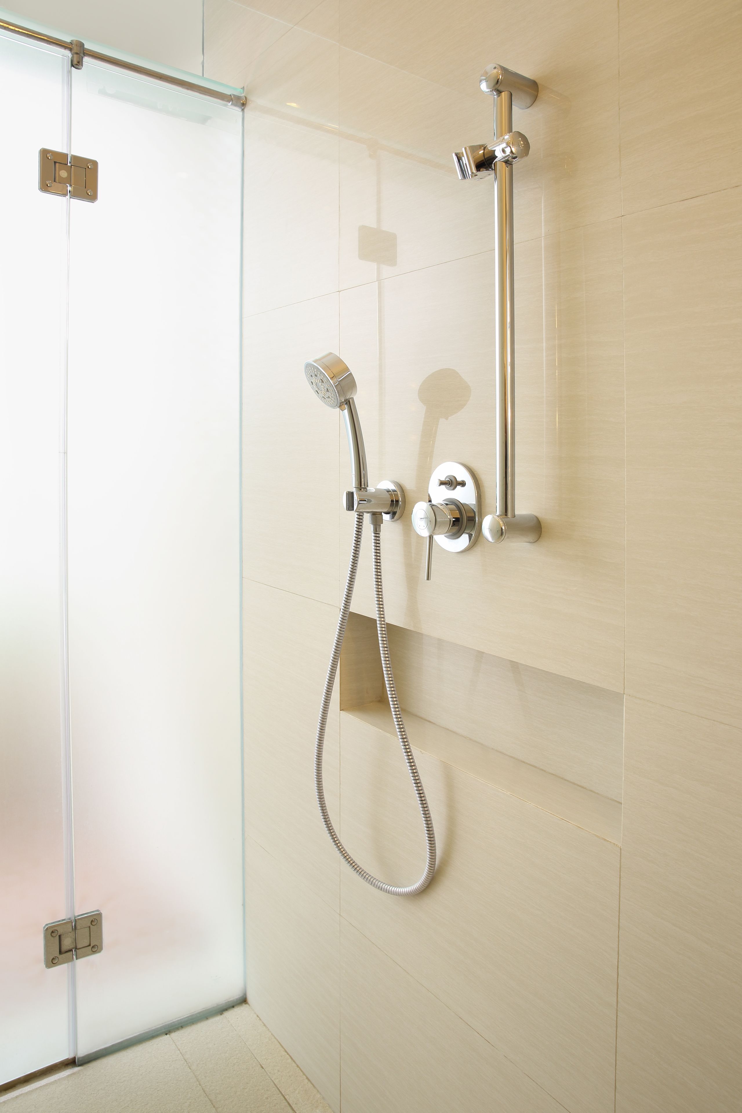 A shower with a handheld showerhead and a wall-mounted faucet, mounted on a tiled wall.
