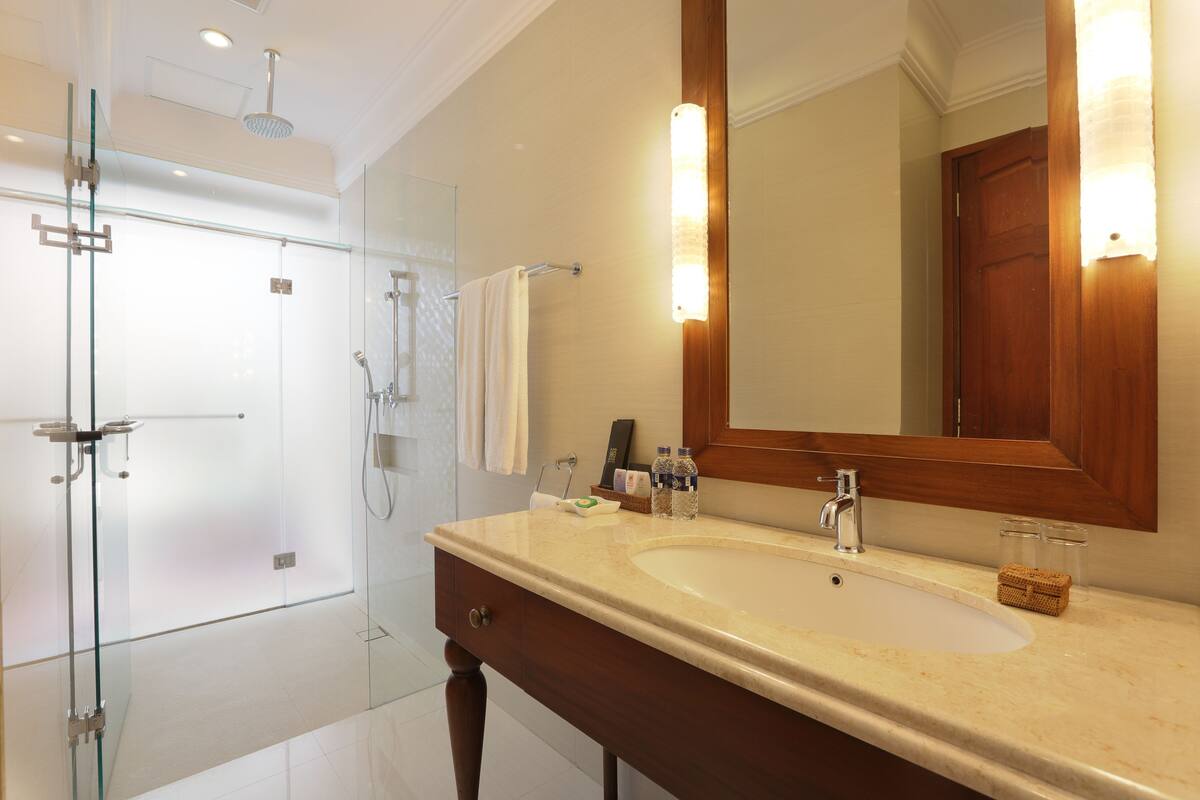 A bathroom with a glass shower enclosure, a sink with a wooden vanity, and a mirror with wall sconces.