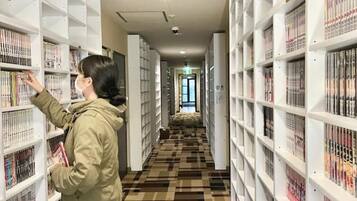 Una persona con chaqueta verde hojea estanterías llenas de libros en una biblioteca con piso estampado.