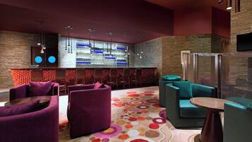 A modern lounge area with purple and teal seating, a bar with blue lighting, and a patterned carpet.
