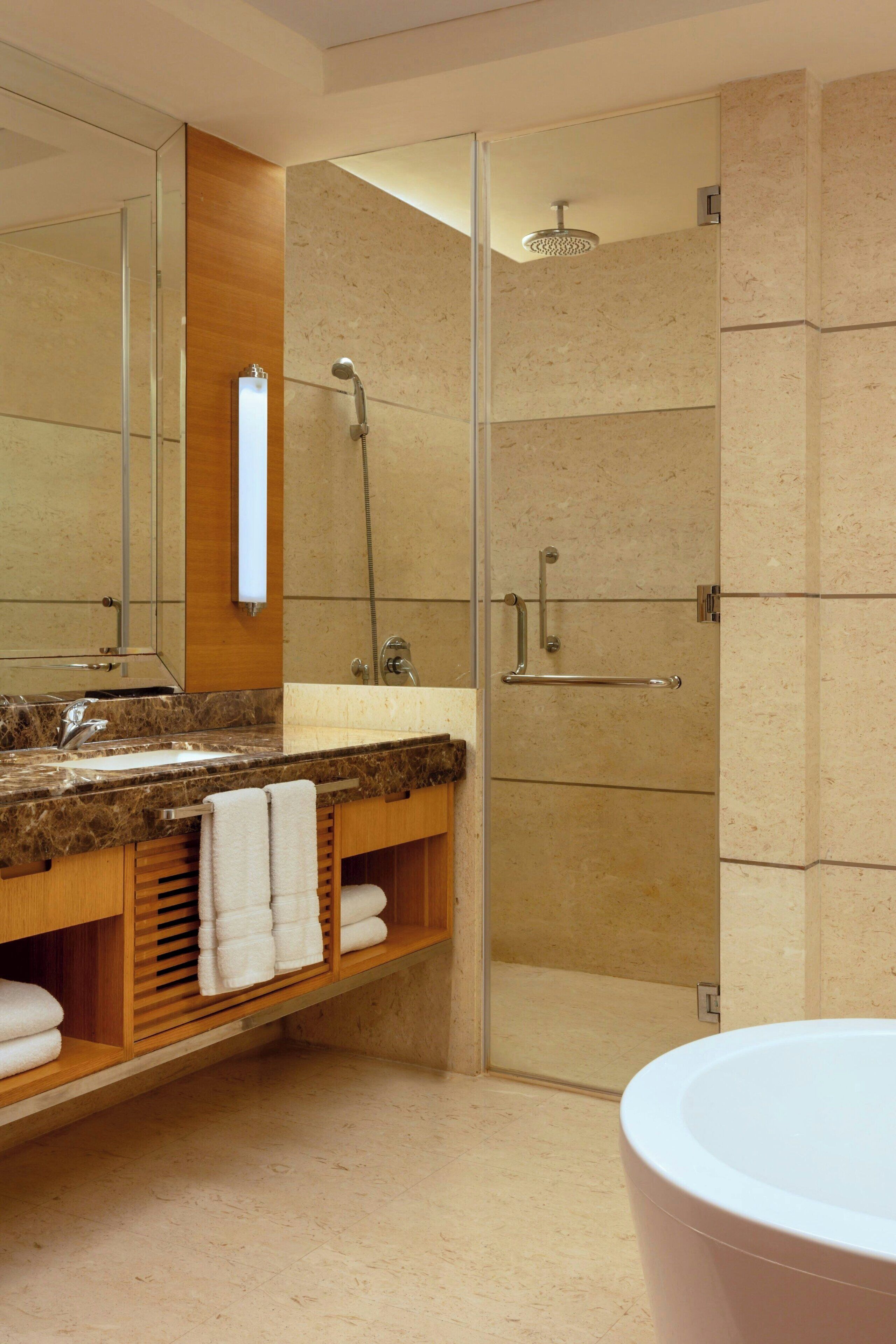 Un baño moderno con lavamanos de granito, un espejo grande, ducha con mampara de vidrio y una bañera blanca.