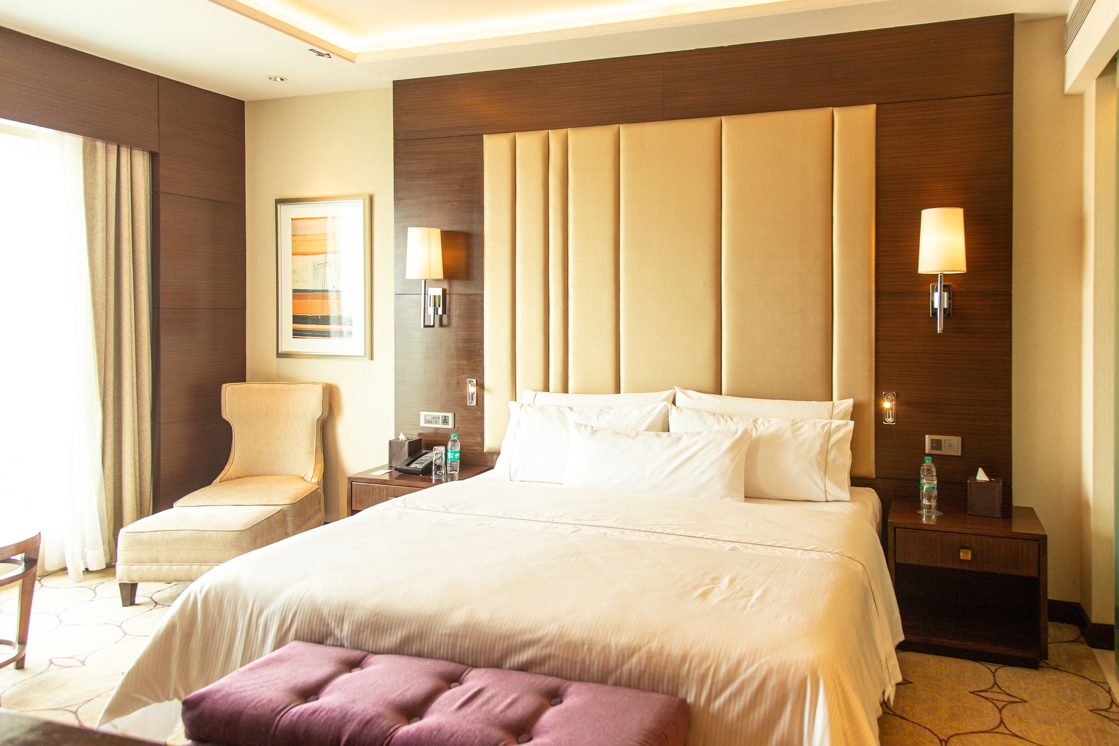 Habitación de hotel con una cama grande, una silla, una mesita de noche y una lámpara fijada a la pared.