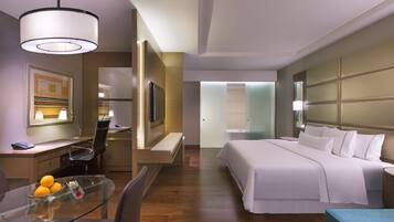 A hotel room with a bed, a desk with a chair, a glass table with fruit, and a TV.
