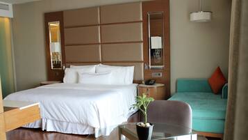 A hotel room with a large bed, a glass table, a small plant, a sofa, and a mirror.