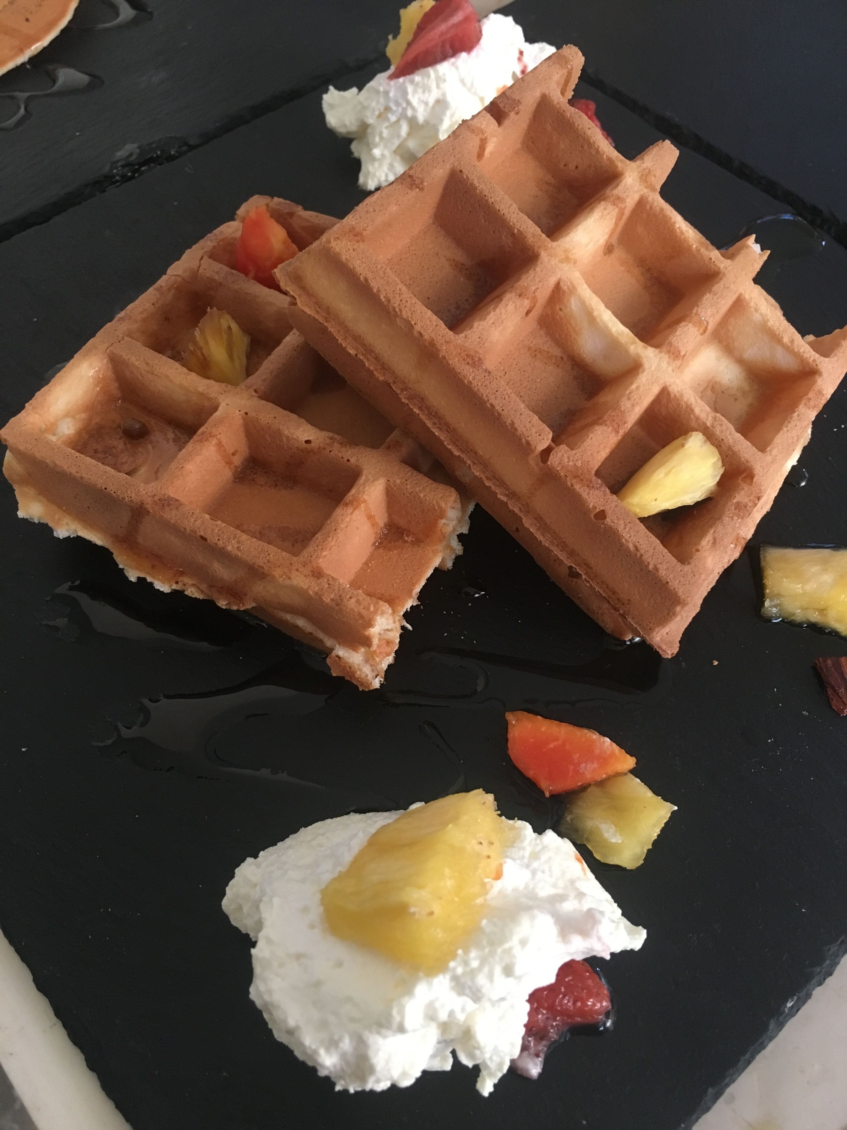 Two waffles with fruit and whipped cream on a black plate.