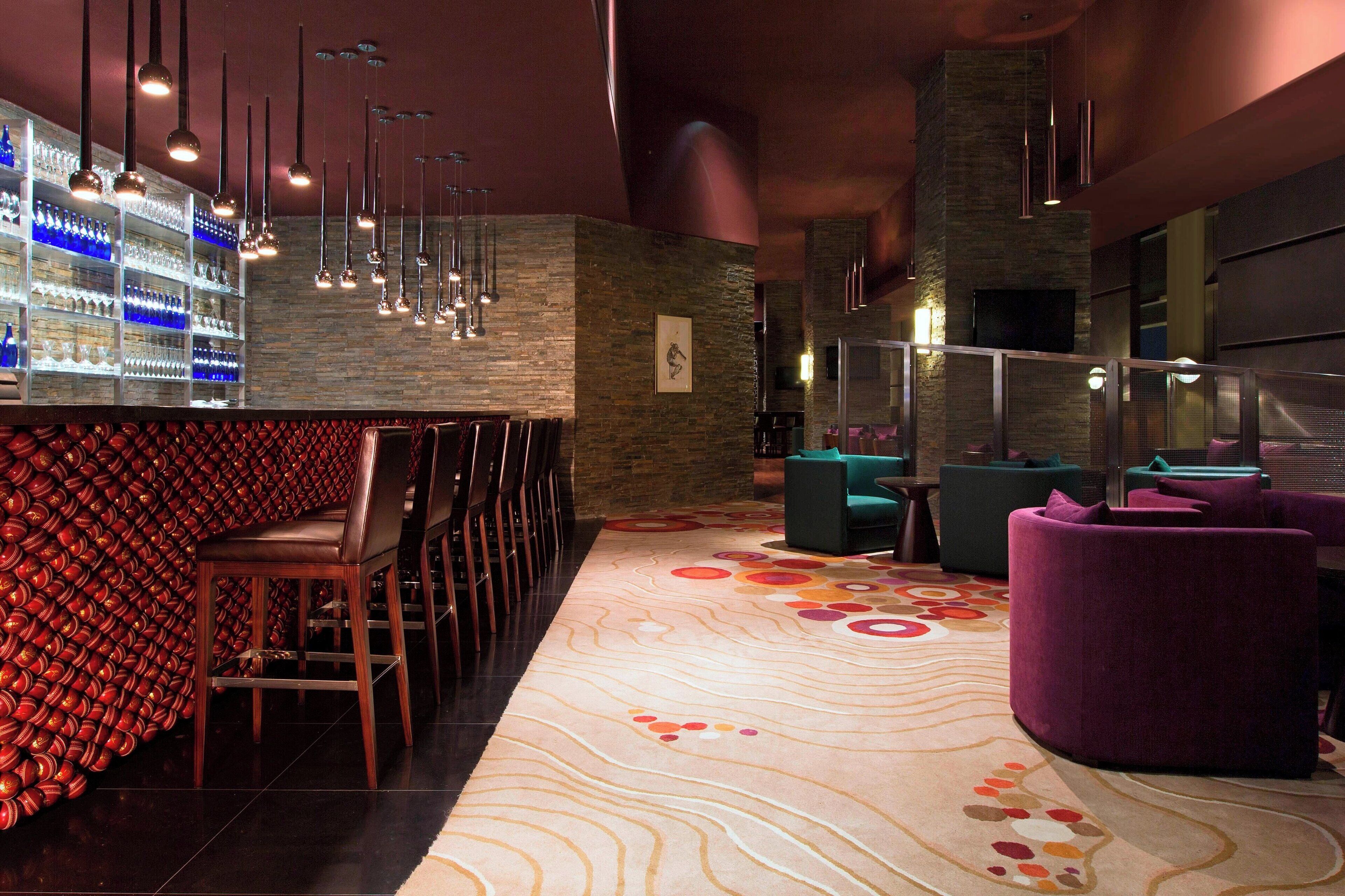 Un espace bar agrémenté d’un tapis à motifs, de sièges et de luminaires suspendus.