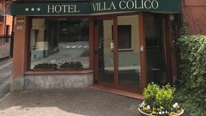 A hotel named "Hotel Villa Colico" with a prominent logo, a balcony with potted plants, and a paved entrance area. - Hotel Villa Colico (Colico)