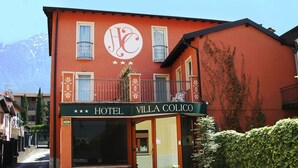 A hotel named "VILLA COLICO" with a red facade, balconies, and a mountain backdrop. - Hotel Villa Colico (Colico)