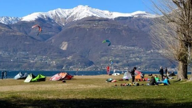 A lakeside view with tents and people, mountains in the background. - Hotel Villa Colico (Colico)