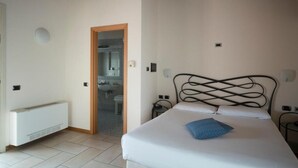 A bedroom with a bed, a radiator, a door leading to a bathroom, and a ceiling with exposed beams. - Hotel Villa Colico (Colico)