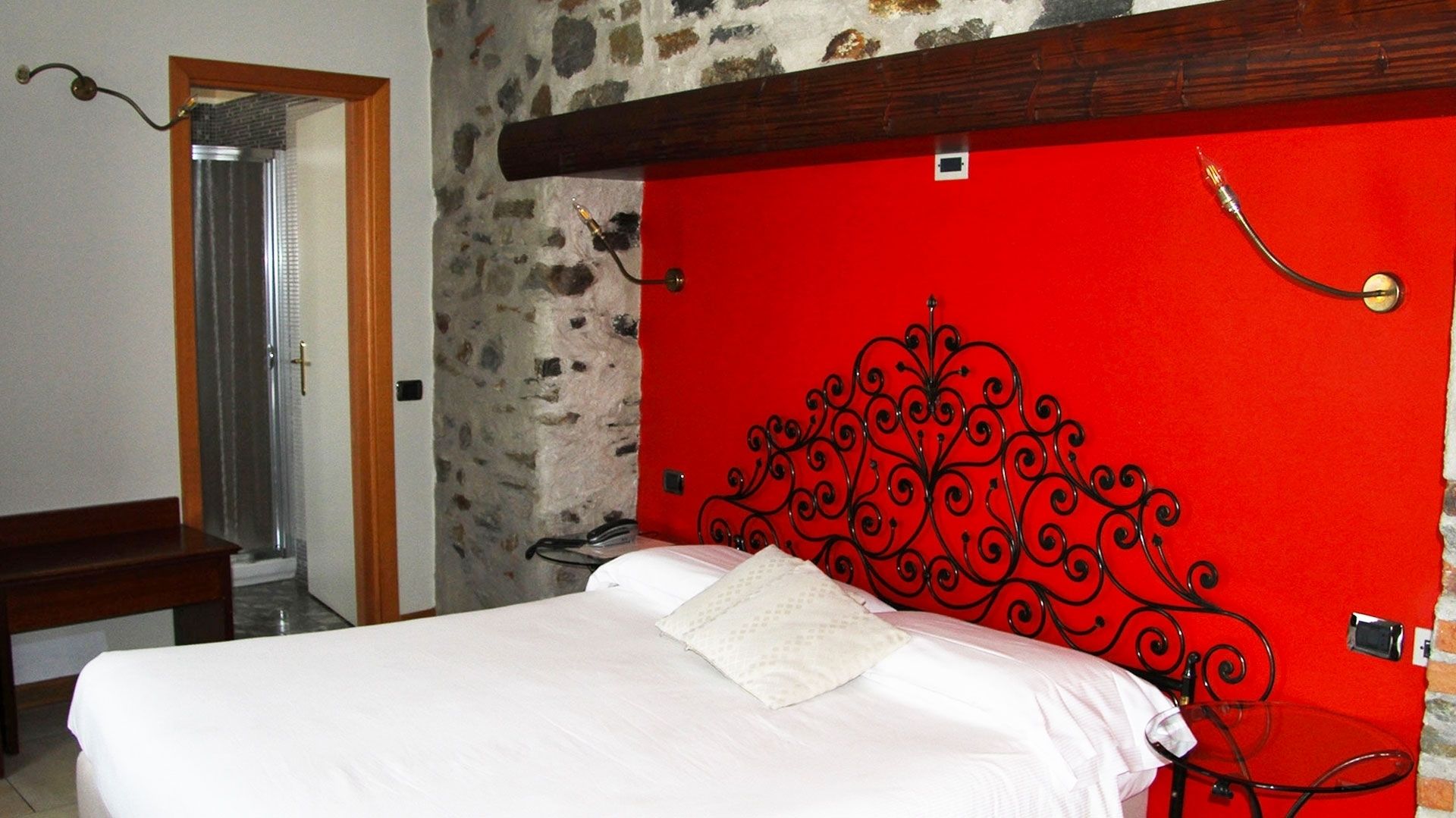 A bedroom with a stone wall, a red headboard, and a wooden bench.