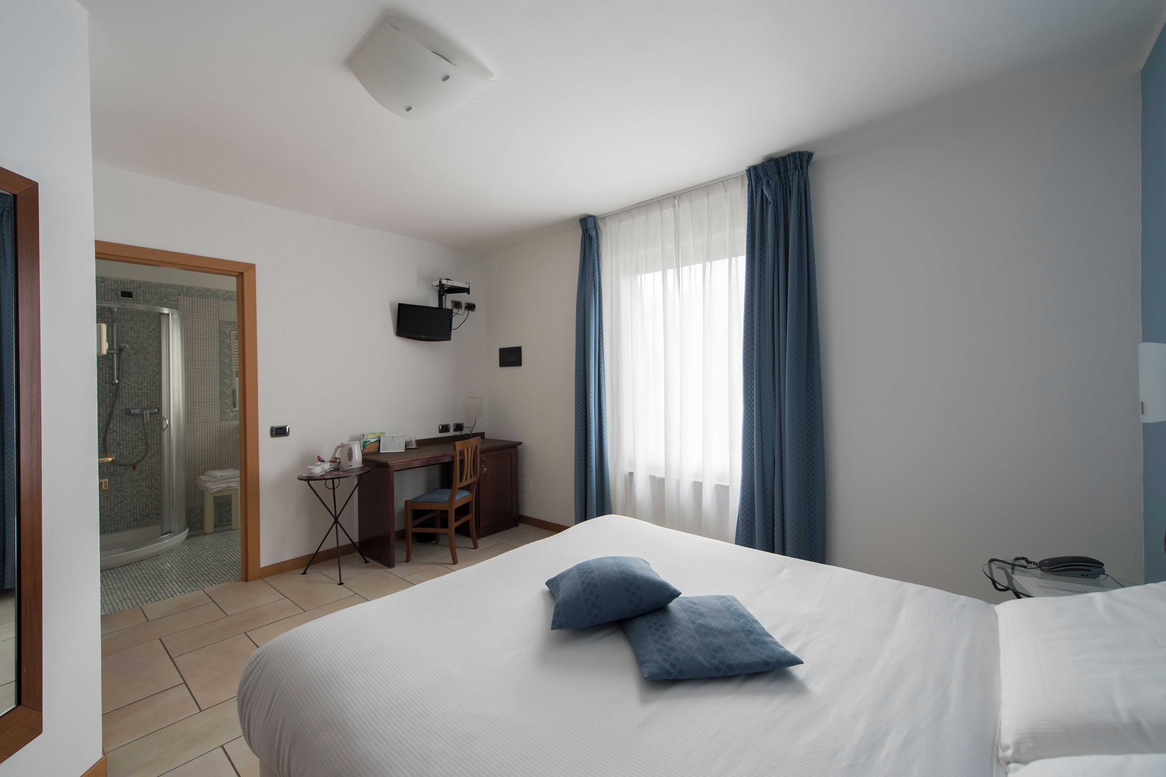 A hotel room with a bed, a desk, a chair, a shower, and a TV.