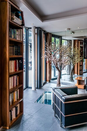 A modern library interior with bookshelves, a black leather couch, and a glass table.