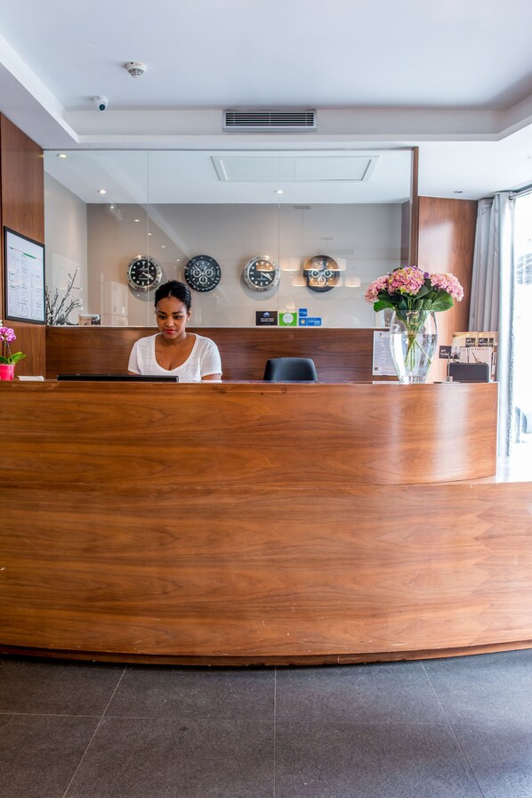 A reception desk with a wooden finish, a vase with flowers, and wall clocks. - Art Hotel Eiffel (Paris)