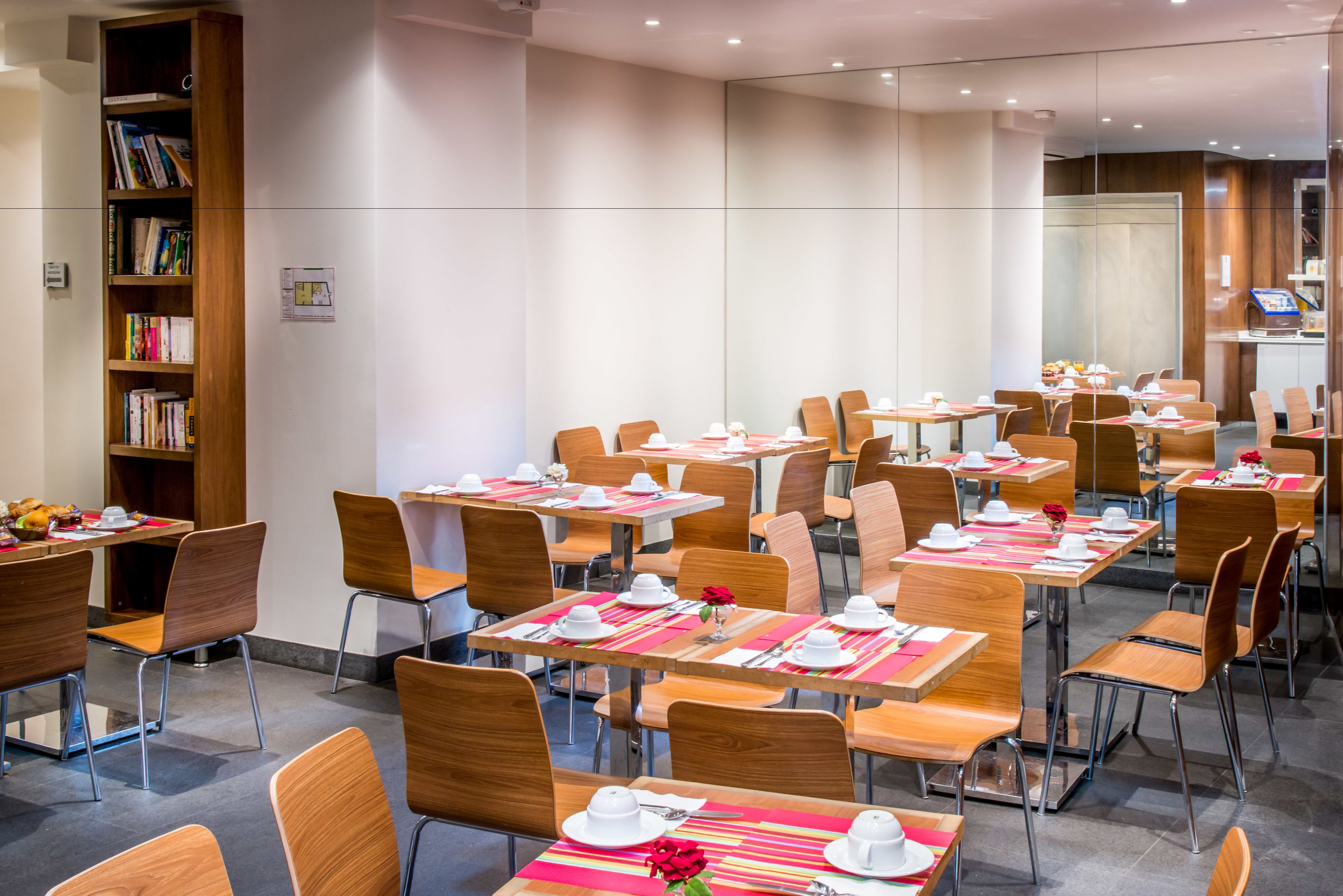 A dining area with multiple tables and chairs, a bookshelf, and a modern interior design.
