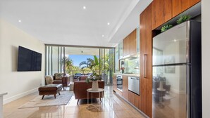 Una cocina moderna con un refrigerador de acero inoxidable, armarios de madera y un amplio ventanal con vistas a un balcón con plantas.