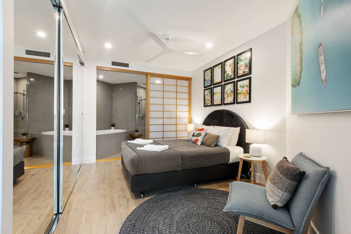 Een moderne slaapkamer met een bed, nachtkastje, stoel en kunstwerk aan de muur.