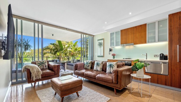 Una sala moderna con un sofá grande, una mesa de centro y vistas a un jardín tropical a través de amplios ventanales.