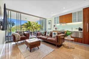 Un salon moderne avec un grand canapé, une table basse et une vue sur un jardin tropical grâce à de grandes fenêtres.