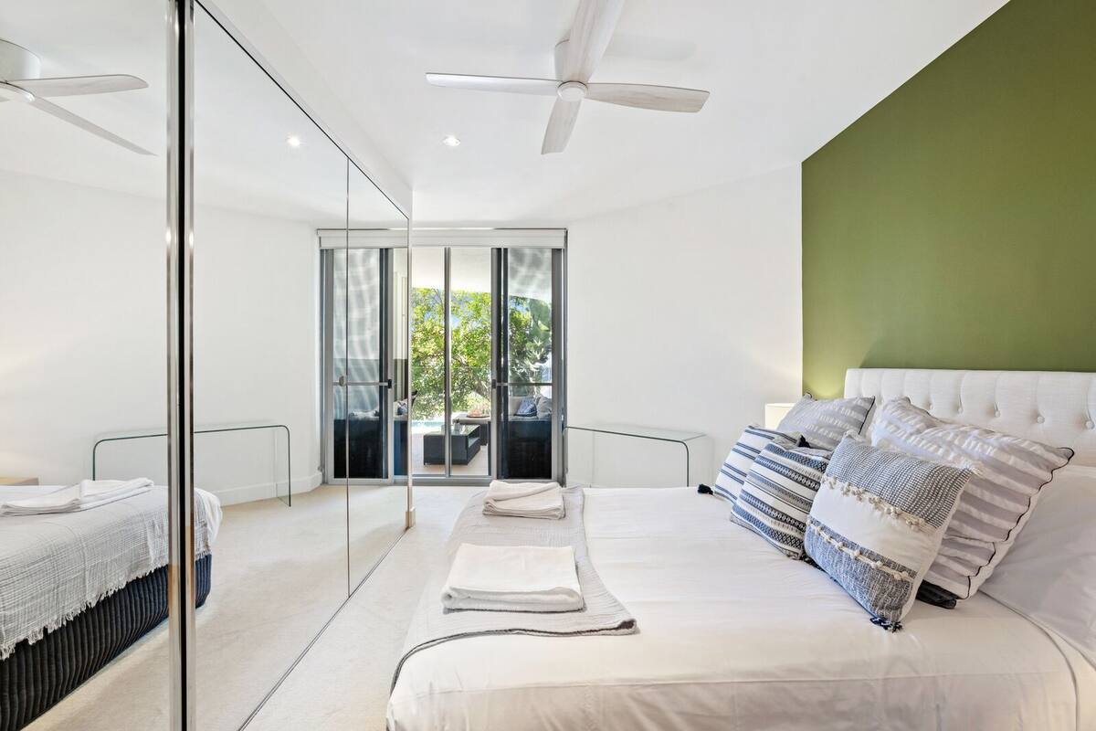 Een moderne slaapkamer met een groot bed, een plafondventilator en een schuifdeur naar een buitenruimte.