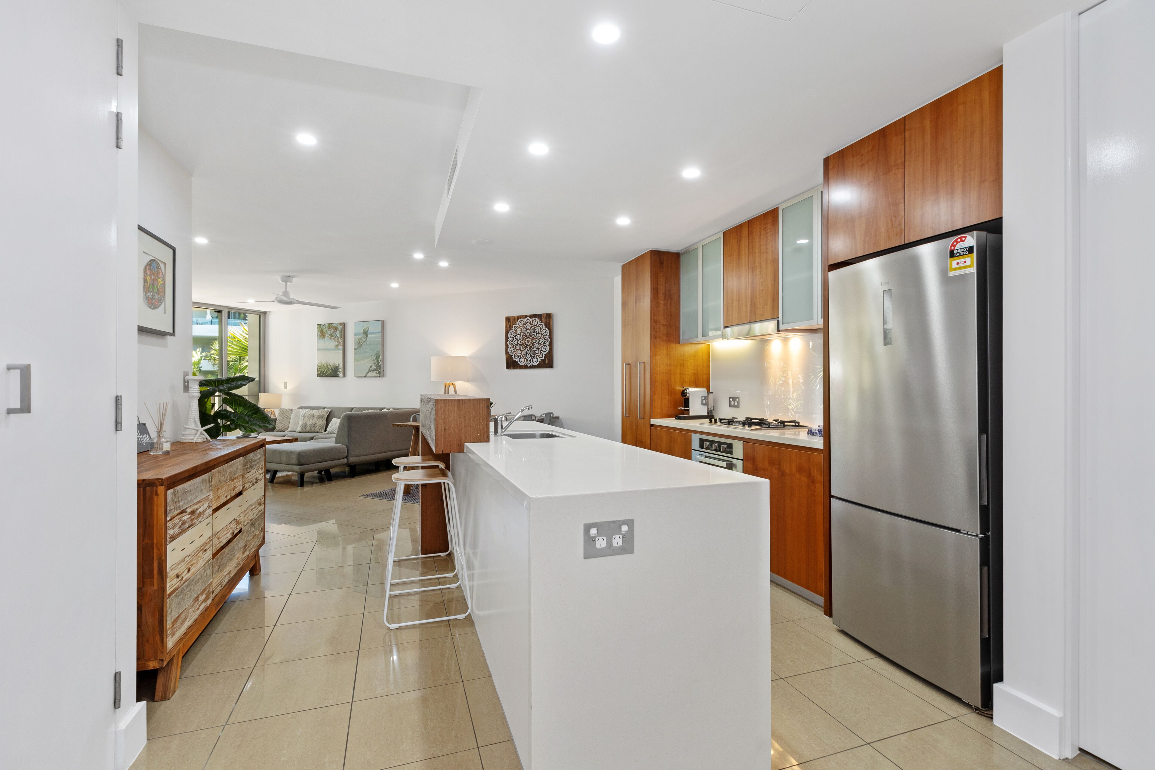 A modern kitchen with a central island, wooden cabinets, stainless steel appliances, and a dining area with a sofa and table.