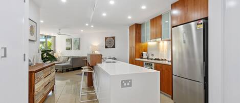 A modern kitchen with a central island, wooden cabinets, stainless steel appliances, and a dining area with a sofa and table.