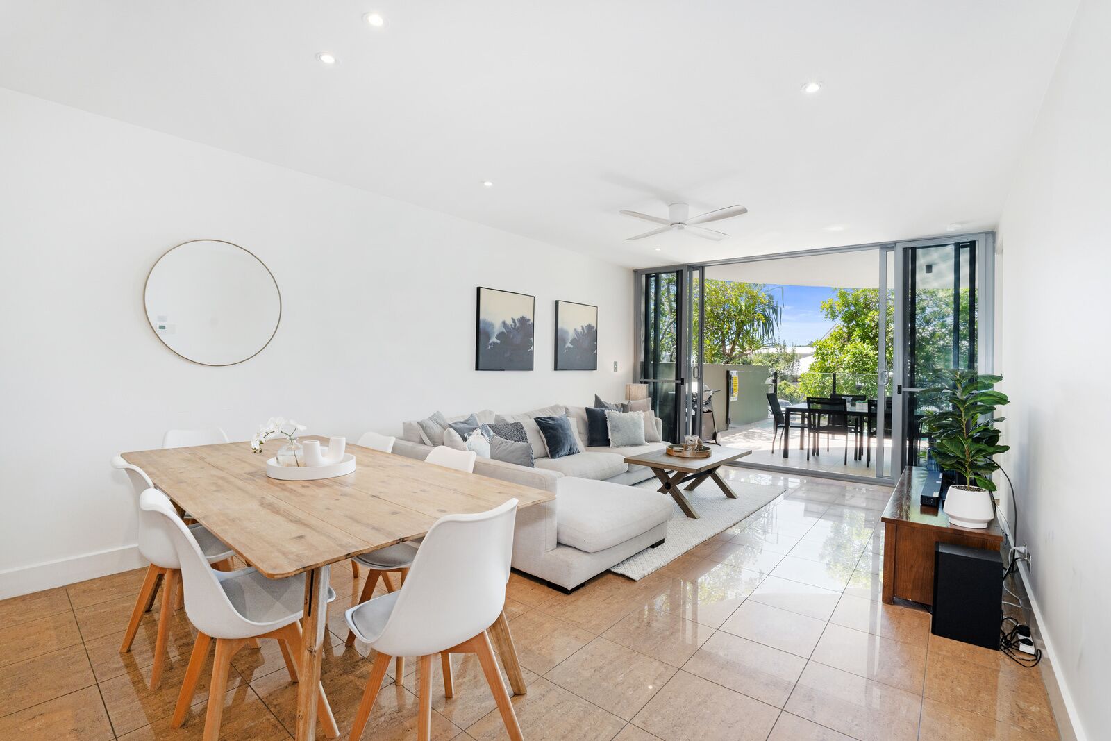 A modern living room with a dining area, a sofa set, and a large sliding glass door leading to an outdoor patio.