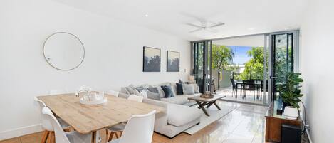 A modern living room with a dining area, a sofa set, and a large sliding glass door leading to an outdoor patio.