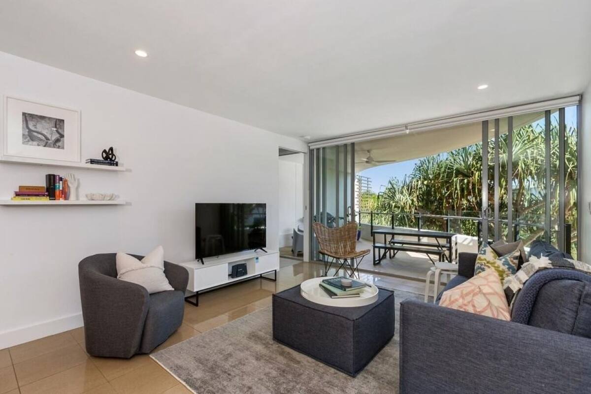 Een moderne woonkamer met een flatscreen televisie, grijze banken, een salontafel en een balkon met tuinmeubilair.