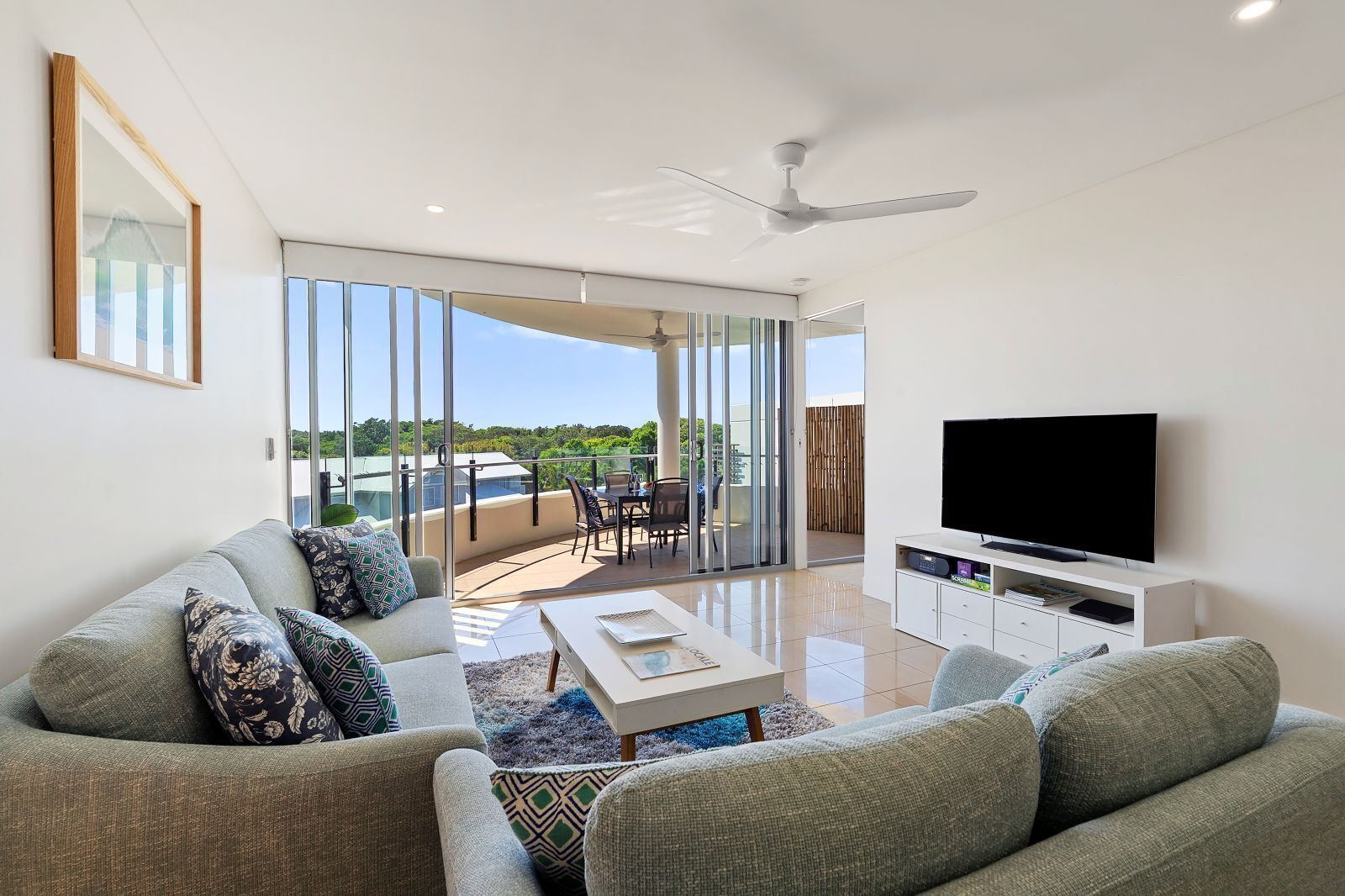 A modern living room with a sofa, TV, and a balcony with a table and chairs.