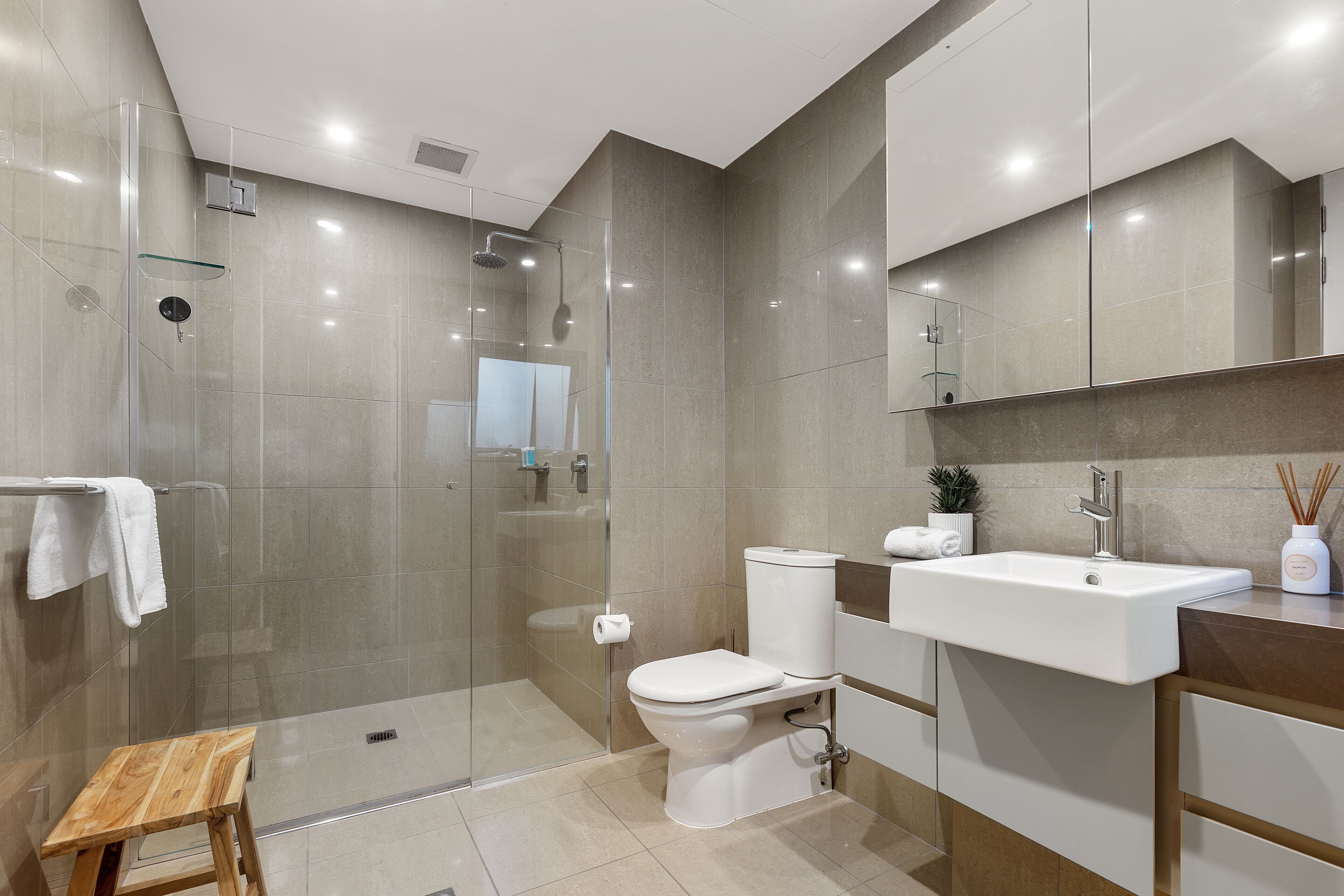 A modern bathroom with a glass-enclosed shower, a white toilet, and a sink with a mirror above.