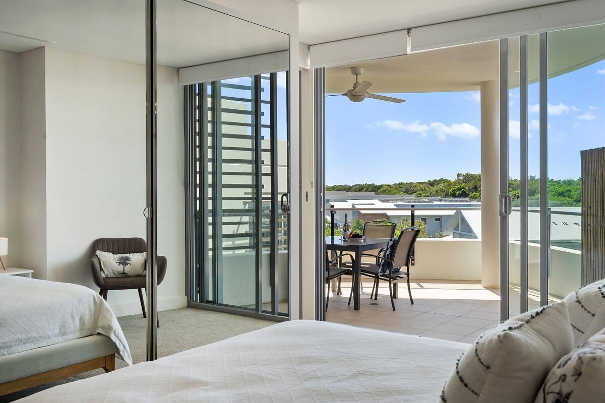 Een hotelkamer met een bed, een stoel, een balkon met een tafel en stoelen, en uitzicht op het landschap.