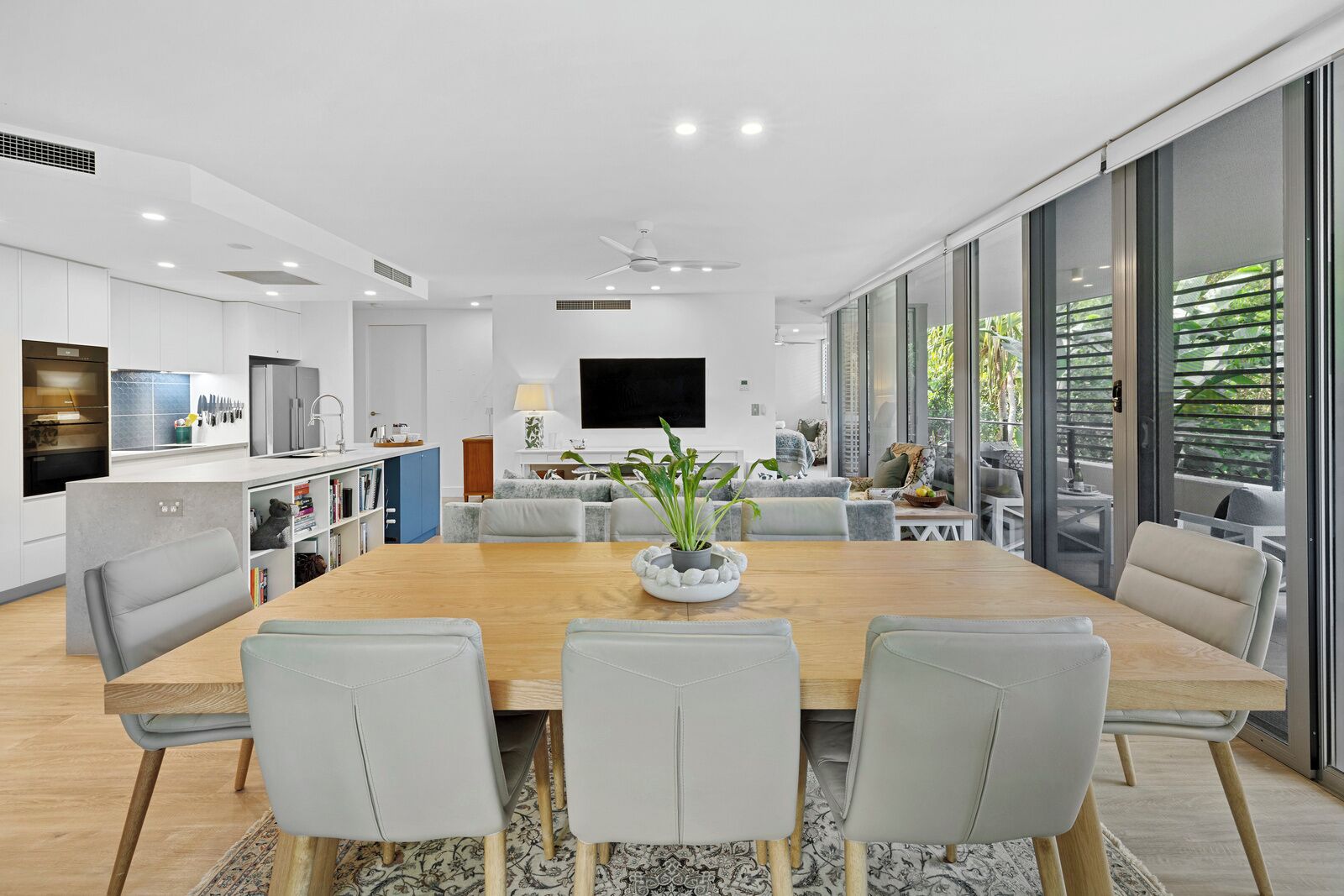 A modern kitchen with white cabinets, a built-in oven, and a dining area with a wooden table and grey chairs.