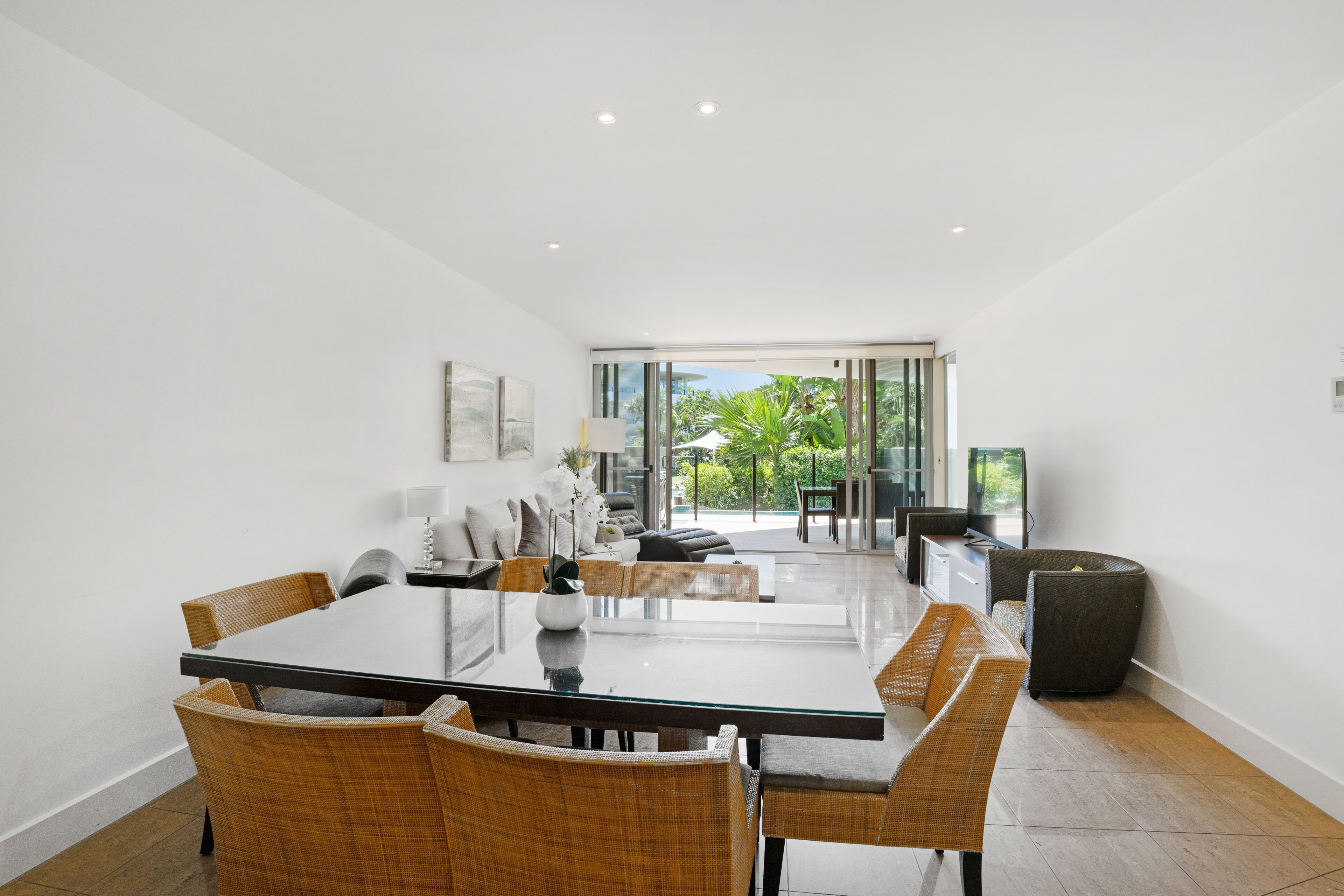 A modern dining area with a glass table, wicker chairs, and a view of the outdoors.