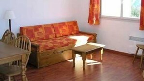 A room with a wooden sofa, a small table, and a chair. There is a window with curtains. - Les Hauts Plateaux (Ax-les-Thermes)