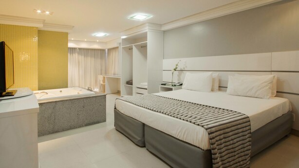 A modern hotel room with a large bed, a separate bathroom with a bathtub, and a vanity with a mirror. - Brisa Tower Hotel (Ceilandia)
