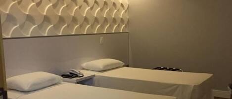 A hotel room with two single beds, a small table, and a wall-mounted air conditioner.