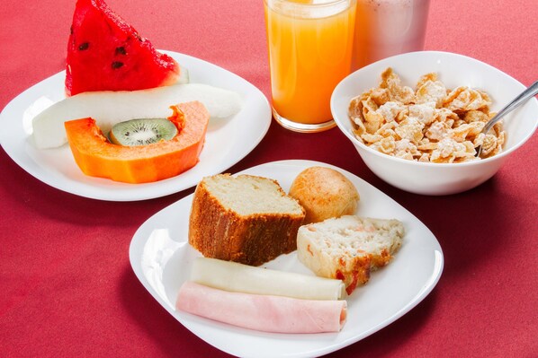Desayuno con platos de comida, incluyendo pan, queso y fruta, además de un vaso de jugo de naranja.
